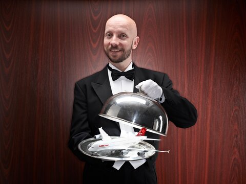 Butler presenting a model airplane on a silver tray indoors