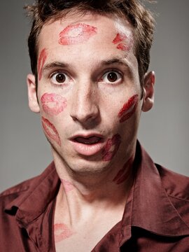 Portrait of embarrassed man with red lipstick kiss showing shock