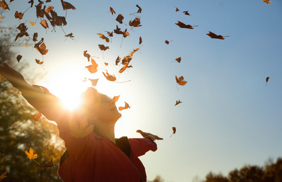 Woman throwing up autumn leaves at backlight