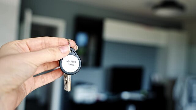 Woman holding house keys with My First Home keychain inside modern apartment interior. Property ownership and first home purchase concept for new homeowners and independent living