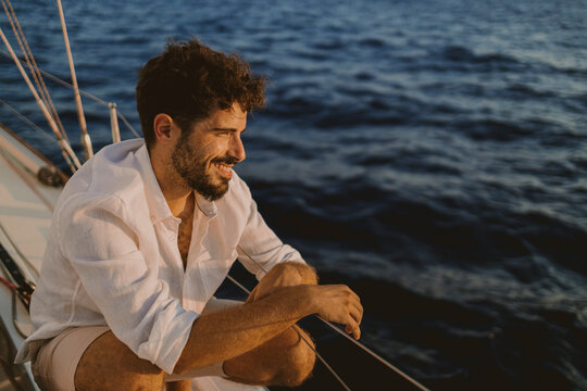 Smiling sailor relaxing on a sailboat at sea during sunset