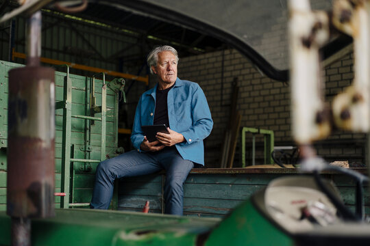 Senior man with tablet sitting on a trailer in barn