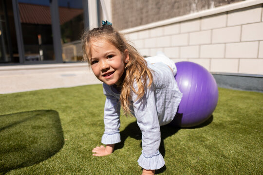 Girl smiling and balancing on a purple fitness ball outdoors