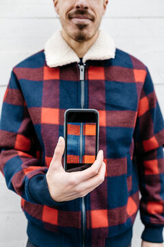 Young man showing a photo on the phone in the colors of his jacket