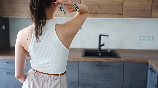 Young woman with apartment keys standing in furnished resale apartment kitchen. Secondary housing purchase and moving into existing property concept