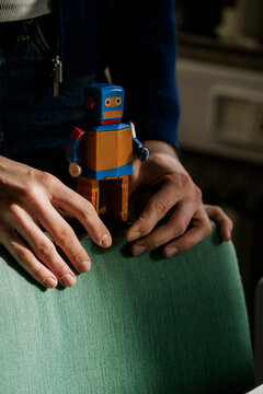 Hands resting on a green chair with a vintage toy robot at home