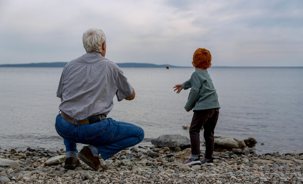 Grandfather with grandson throwing pebble into sea at beach