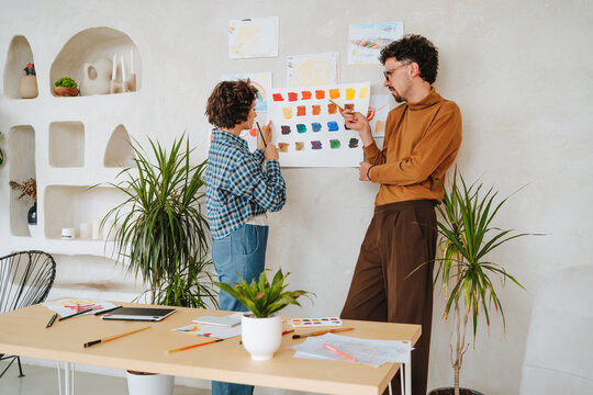 Graphic designer discussing with colleague over color swatch on wall at office