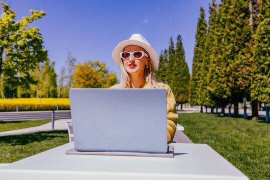 Happy freelancer working on laptop at outdoor park cafe in spring