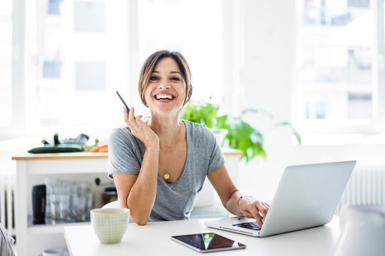 Happy oman sitting at desk, working from home, using laptop