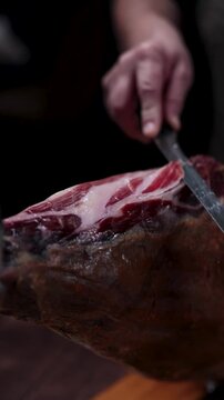 Hand slicing thin delicate pieces of delicious serrano ham from a whole cured pork leg