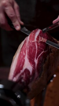 Hand slicing thin delicate pieces of delicious serrano ham from a whole cured pork leg