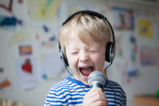 Portrait of singing little boy with headphones and microphone