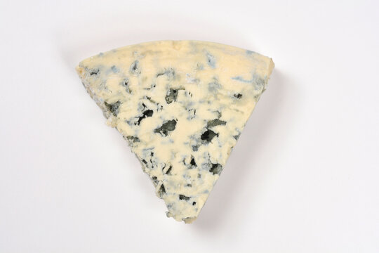 A top down view of a triangular piece of traditional Danish Blue cheese (Danablu) with distinct mold veins on a plain white surface.
