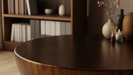 Diffuser and glass candle with flower vase on round wooden table across bookshelf in cafe or library. © bongkarn