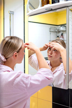 Woman applying face tape on forehead in bathroom mirror