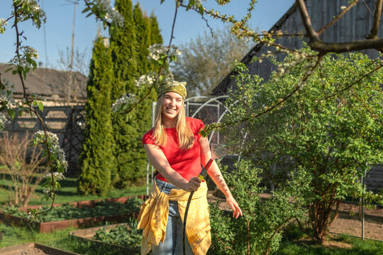 Smiling gardener watering blooming trees in sunny backyard