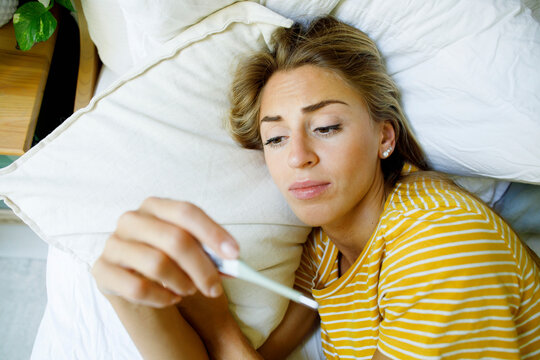 ill woman checking temperature with thermometer in bed at home
