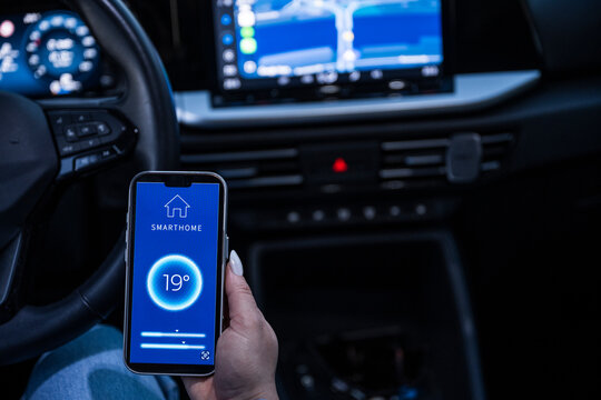 Hand using smarthome app on smartphone inside a modern car