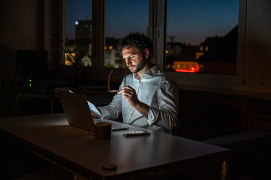Businessman working late at night in dark office with tablet