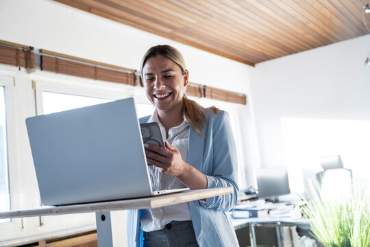Smiling professional standing at office desk reading smartphone