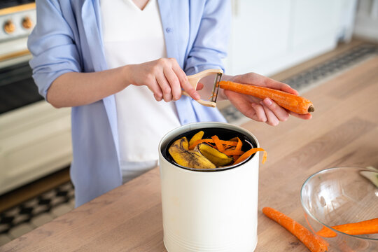 Woman peeling carrot peel in compost bin at home