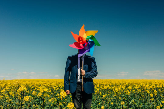 Businessman hiding face with colorful pinwheel in rapeseed field