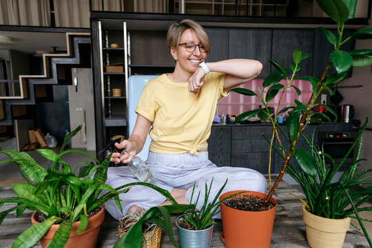 Happy woman using smart watch and watering plants at home