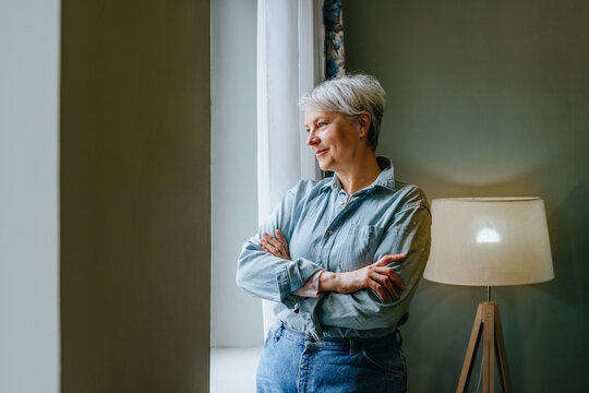 Woman with arms crossed looking through window thoughtfully