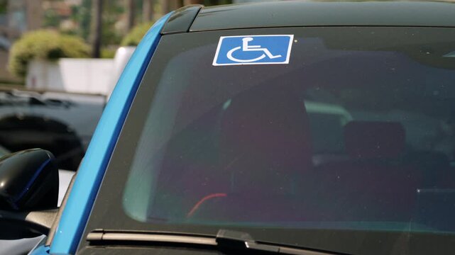 Handicap parking permit displayed on a blue parked car windshield in city street