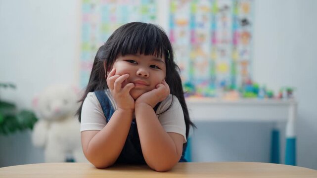 Cute Asian Little Girl Showing Different Facial Expressions While Sitting at Table Indoors