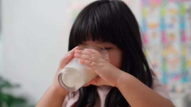 Cute Asian Little Girl Drinking Milk During Breakfast at Home