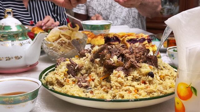Uzbek family at festive Eid table with plov, tea and samsa, close-up