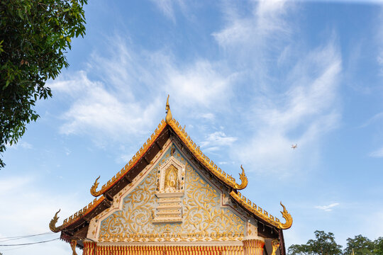 The golden and blue decorated gable roof of a traditional Thai Buddhist temple under a clear blue sky.