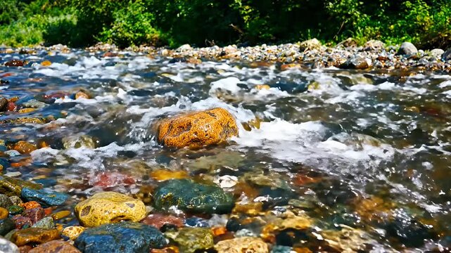 Clear water flowing over colorful river stones. Fast stream. Wet rocks stream pebbles flow.
