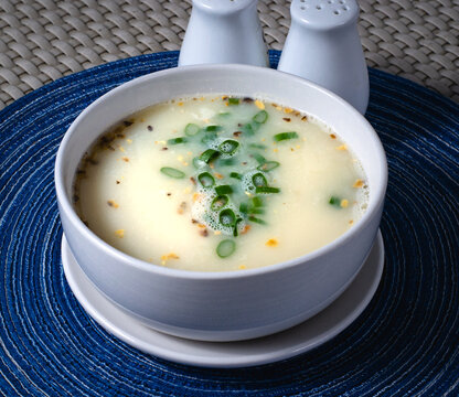 close up photo of crab and corn soup with spring onions and fried garlic as garnish on a white bowl.
