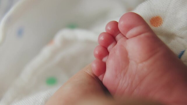 Newborn's Delicate Foot: A close-up of a newborn baby's tiny, soft foot, held gently by an adult hand, nestled on a patterned blanket. Symbol of new life and tender moments.