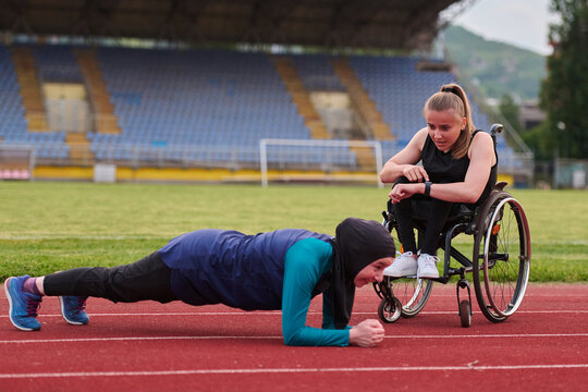 Determined Wheelchair Athlete Coaching Friend During Outdoor Fitness Training On Track Stadium