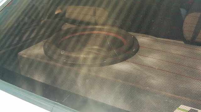 View of powerful subwoofer speaker inside custom wooden box, installed in vehicle trunk, observed through rear window with defroster lines. Setup provides enhanced car audio bass.