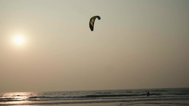Lone kitesurfer enjoys a session on the ocean during a beautiful sunset, gliding across the water with a colorful kite flying high in the golden sky, creating a serene and adventurous scene