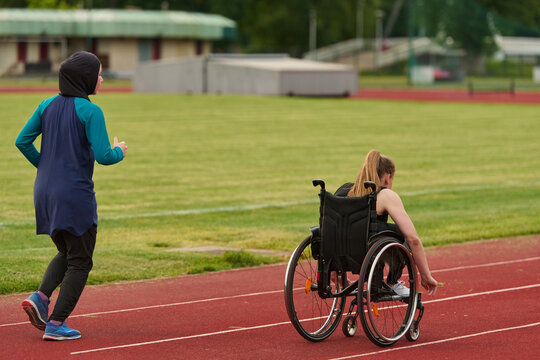 Female Wheelchair Athlete Training On Track With Running Partner Wearing Hijab Inclusive Sports