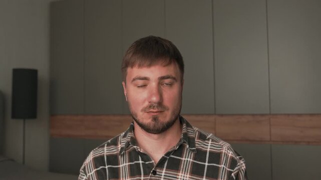 A man in a plaid shirt straightens his hair on his head. A man adjusts his hair at home.