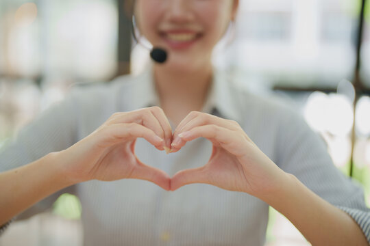 Call center employee wearing headset forming an adorable heart shape with hands, showing care and excellent customer service with a friendly smiling face