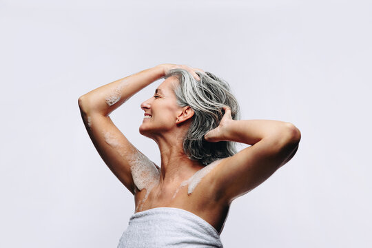 Mature woman washing hair and smiling in studio