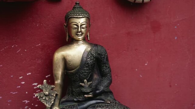 Brass meditating Buddha statue with closed eyes exuding calm and enlightenment, set against a textured vibrant red wall symbolizing energy, passion and spiritual depth
