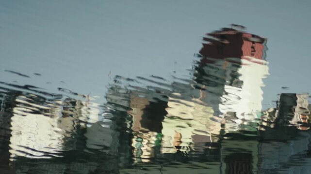 Distorted reflection of colorful buildings creating an impressionistic and abstract pattern on the rippling surface of the water, evoking a sense of calm and tranquility in a dynamic motion