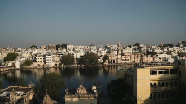 Panoramic view panning across the historic city of Udaipur, revealing traditional Indian architecture, ancient ghats, and the serene waters of Lake Pichola under a clear morning sky