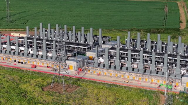 Close up aerial view of a flexible generation power plant showing symmetrical rows of electrical transformers and industrial chimney stacks in Essex, UK.