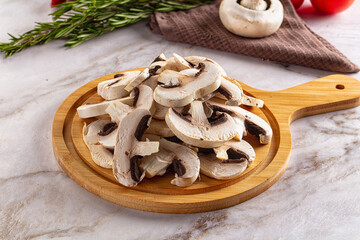 Fototapeta premium Sliced fresh mushrooms on wooden cutting board with rosemary and whole mushroom