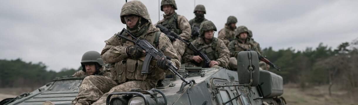 Troopers on the Move: A troop of soldiers in full combat gear, armed with rifles, ride atop a military vehicle.